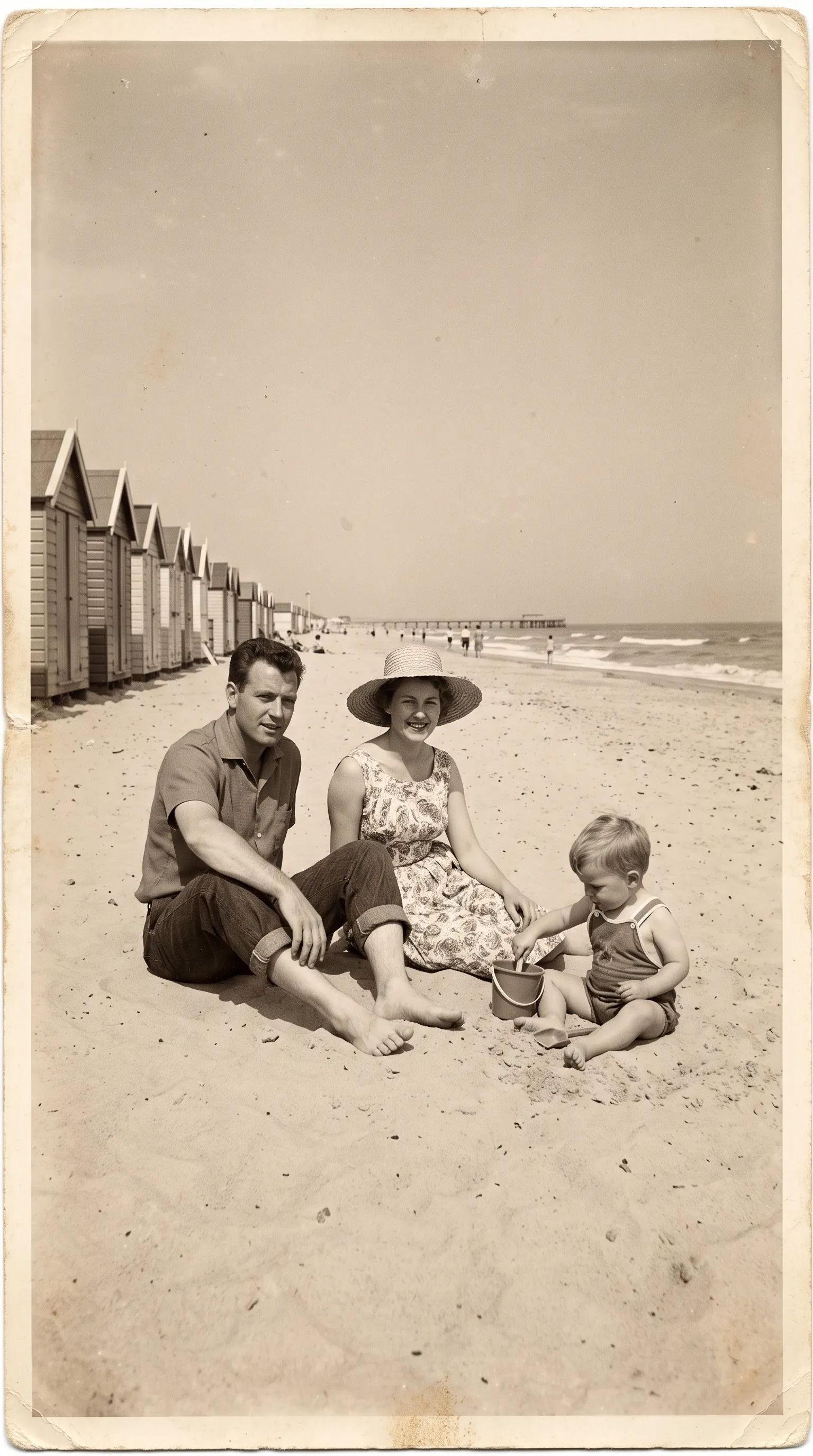 Sepia 1960s photo of a family of three sitting on the sand at the seaside