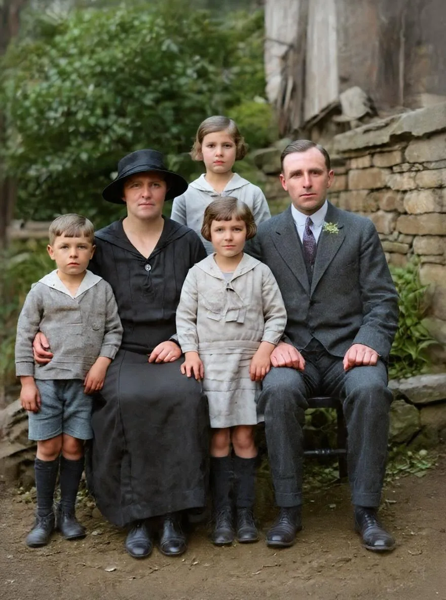 Restored black-and-white portrait of a family of five standing in front of a stone wall